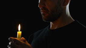 Young man looking to heaven and blowing candle, blessing God, dark background
