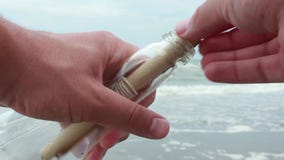 Young man opening message in a bottle on sand beach