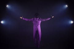 Young man in purple suit standing on the background of the spotlight. Showman spreading hands, show begins