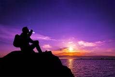 Young man silhouette drinking water on the stone at sunset stock photography Young man silhouette drinking water on the stone at sunset stock photography