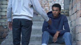 Young man stretching out hand to sad friends sitting stairs, friendship support