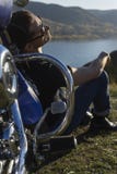 Young man wearing a black leather jacket, sunglasses and jeans s. Its outdoor on a ground at a motorcycle, resting on a mountain above the river. Lifestyle stock photos Young man wearing a black leather jacket, sunglasses and jeans s. Its outdoor on a ground at a motorcycle, resting on a mountain above the river. Lifestyle stock photos