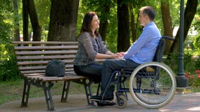Young man on wheelchair talking with his wife in park stock video Young man on wheelchair talking with his wife in park stock video