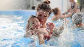 Young mom in the pool playing with her baby daughter in slow motion. Sports family engaged in an active lifestyle