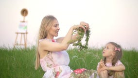 Young mother puts on wreath on her head and little daughter sitting on the summer meadow recreation outdoors stock footage Young mother puts on wreath on her head and little daughter sitting on the summer meadow recreation outdoors stock footage