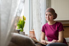 Young positive adult female cancer patient sitting in the kitchen by a window reading a book, smiling. stock images Young positive adult female cancer patient sitting in the kitchen by a window reading a book, smiling. stock images