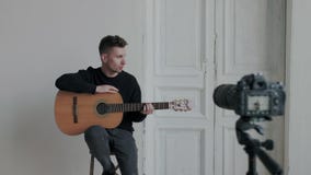 Young pretty musician blogger is recording tutorial about playing guitar for internet blog using professional camera. He stock video footage Young pretty musician blogger is recording tutorial about playing guitar for internet blog using professional camera. He stock video footage