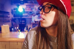 Young pretty woman in red cap smoke an electronic cigarette at the vape shop. Closeup. stock photo Young pretty woman in red cap smoke an electronic cigarette at the vape shop. Closeup. stock photo