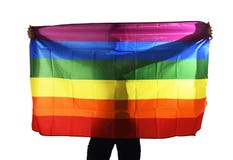 Young proud gay man spreading wide big pride homosexual flag with his shadow behind the cloth stock image Young proud gay man spreading wide big pride homosexual flag with his shadow behind the cloth stock image