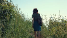 Red-haired girl in a cowboy hat with a backpack walks on a mountain trail. stock footage Red-haired girl in a cowboy hat with a backpack walks on a mountain trail. stock footage