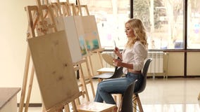 A young sexy girl in a white shirt draws on canvas in the studio for drawing. stock footage A young sexy girl in a white shirt draws on canvas in the studio for drawing. stock footage