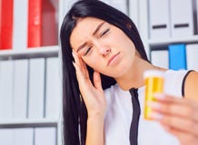 Young beautiful tired sick woman sitting in workplace in office holding bottle with pills. Female feeling bad at work. stock photo Young beautiful tired sick woman sitting in workplace in office holding bottle with pills. Female feeling bad at work. stock photo