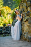 A young sexy bride with circlet of flowers posing and smiling standing on wooden stairs near rock fence stock images A young sexy bride with circlet of flowers posing and smiling standing on wooden stairs near rock fence stock images