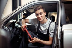 A young smiling automechanic is sitting in a car with a special device for cheching the computer system of a car royalty free stock image A young smiling automechanic is sitting in a car with a special device for cheching the computer system of a car royalty free stock image
