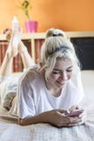 Young smiling beautiful brunette woman lies with phone in big white bed. royalty free stock images Young smiling beautiful brunette woman lies with phone in big white bed. royalty free stock images