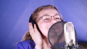 A young smiling woman in headphones singing song in the studio. Mid shot A young smiling woman in headphones singing song in the studio. Mid shot