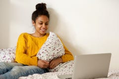 Young smiling woman sitting with laptop on bed Stock Photo Young smiling woman sitting with laptop on bed Stock Photo