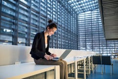 Young Student Or Businesswoman Sitting On Desk In Room In A Library Or Office, Using Laptop. Royalty Free Stock Photos Young Student Or Businesswoman Sitting On Desk In Room In A Library Or Office, Using Laptop. Royalty Free Stock Photos