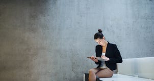 Young Student Or Businesswoman Sitting On Desk In Room In A Library Or Office, Using Tablet. Stock Photo Young Student Or Businesswoman Sitting On Desk In Room In A Library Or Office, Using Tablet. Stock Photo
