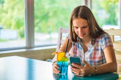Young teenager brunette girl with long hair sitting indoor in urban cafe, drink a blue lemonade cocktail and use her smartphone stock photos Young teenager brunette girl with long hair sitting indoor in urban cafe, drink a blue lemonade cocktail and use her smartphone stock photos