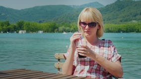 Young tourist woman relaxing in a beautiful location by the lake and mountains in Spain. Drinks Coke from a glass with a stock footage Young tourist woman relaxing in a beautiful location by the lake and mountains in Spain. Drinks Coke from a glass with a stock footage