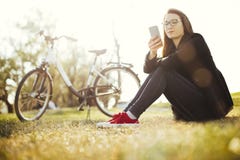 Young woman with bicycle relaxing sitting on grass using smart phone in park royalty free stock photos Young woman with bicycle relaxing sitting on grass using smart phone in park royalty free stock photos