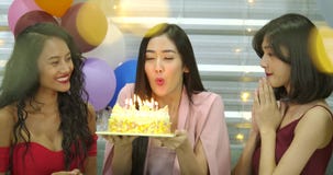 Young woman birthday girl is making wish, blowing candle on cake and clapping hands while her friends are congratulating stock video footage Young woman birthday girl is making wish, blowing candle on cake and clapping hands while her friends are congratulating stock video footage