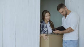 Young woman deliver cardboard box to customer at home. Man sign in clipboard for receiving parcel stock video footage Young woman deliver cardboard box to customer at home. Man sign in clipboard for receiving parcel stock video footage