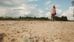 A young woman in a dress rides a bicycle on the background of a field in the village. stock video footage A young woman in a dress rides a bicycle on the background of a field in the village. stock video footage