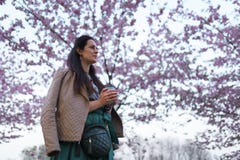 Young woman drinking coffee from a paper cup wearing emerald color skirt - Colorful sakura cherry blossom in a park in royalty free stock photos Young woman drinking coffee from a paper cup wearing emerald color skirt - Colorful sakura cherry blossom in a park in royalty free stock photos