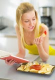Young woman eating chips and reading book
