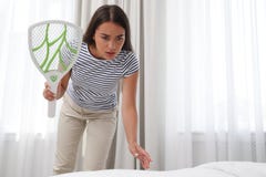 Young woman with electric fly swatter in bedroom. Insect killer