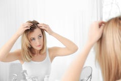 Young woman with hair loss problem looking in mirror
