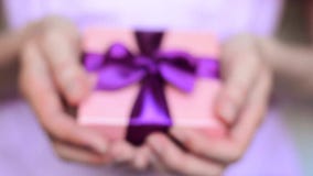 Young woman holds a gift box with a bow close up. Young woman holds a gift box with a purple bow close up Young woman holds a gift box with a bow close up. Young woman holds a gift box with a purple bow close up