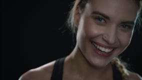 Young woman laughnig in black studio. Close up of fit girl with piercing in nose stock footage Young woman laughnig in black studio. Close up of fit girl with piercing in nose stock footage