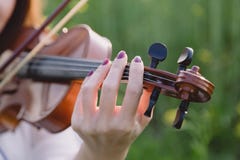 Young woman playing violin in a field at sunset. Young woman playing violin in a green field at sunset. Focus on the hand Royalty Free Stock Images Young woman playing violin in a field at sunset. Young woman playing violin in a green field at sunset. Focus on the hand Royalty Free Stock Images