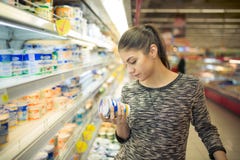 Young woman reading ingredients,declaration or expiration date on a diary product before buying it.Curious woman reading nutrition