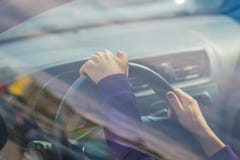 Young woman`s hand holding on black steering wheel while driving in the car. view from the outside of the car stock image Young woman`s hand holding on black steering wheel while driving in the car. view from the outside of the car stock image