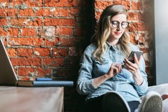Young woman sits in cafe on windowsill and uses smartphone. Hipster girl checking e-mail, chatting, blogging, working. stock photography Young woman sits in cafe on windowsill and uses smartphone. Hipster girl checking e-mail, chatting, blogging, working. stock photography