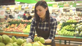 Young woman store worker in a brown apron at the department with fruits and vegetables stock footage Young woman store worker in a brown apron at the department with fruits and vegetables stock footage
