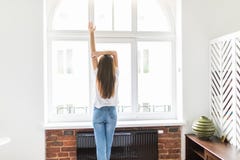Young woman stretching in the bedroom at the window after wake up. Rear view, girl in the bedroom looks out the window with his Ar royalty free stock image Young woman stretching in the bedroom at the window after wake up. Rear view, girl in the bedroom looks out the window with his Ar royalty free stock image