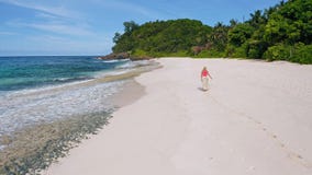 Young woman walks on the sand paradise Anse Bazarca beach. Aerial 4k follow footage view. Ocean waves roll to the shore