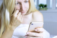 Zamazany uśmiechnięty blond kobiety obsiadanie na łóżku z białą pościelą i używać smartphone obrazy royalty free Zamazany uśmiechnięty blond kobiety obsiadanie na łóżku z białą pościelą i używać smartphone obrazy royalty free