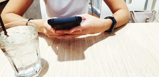 Zamyka w górę kobiety ` s ręki używać czarnego mądrze telefon z szkłem zimna woda na drewnianym stole podczas czekania dla jedzen zdjęcia royalty free Zamyka w górę kobiety ` s ręki używać czarnego mądrze telefon z szkłem zimna woda na drewnianym stole podczas czekania dla jedzen zdjęcia royalty free