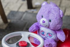 Zartes Bild eines purpurroten Teddybären, der auf einem roten Auto für Kinder sitzt stockbild Zartes Bild eines purpurroten Teddybären, der auf einem roten Auto für Kinder sitzt stockbild
