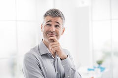 Zekere glimlachende mens die en bij camera stellen glimlachen, denkt hij met hand op kin stock foto's Zekere glimlachende mens die en bij camera stellen glimlachen, denkt hij met hand op kin stock foto's