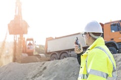 Zijaanzicht van supervisor die walkie-talkie met behulp van bij bouwwerf tegen duidelijke hemel Stock Afbeeldingen Zijaanzicht van supervisor die walkie-talkie met behulp van bij bouwwerf tegen duidelijke hemel Stock Afbeeldingen