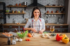 Zit de vrolijke vrouw van Nice bij lijst in keuken Zij die koken De vrouw kijkt op camera en glimlach Zij sneed groene ui op bure royalty-vrije stock foto Zit de vrolijke vrouw van Nice bij lijst in keuken Zij die koken De vrouw kijkt op camera en glimlach Zij sneed groene ui op bure royalty-vrije stock foto