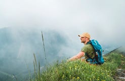Zmęczony backpacker mężczyzna spoczynkową przerwę cieszy się chmurnego doliny dna odprowadzenie mgłowym chmurnym pogodowym pasmem obraz royalty free Zmęczony backpacker mężczyzna spoczynkową przerwę cieszy się chmurnego doliny dna odprowadzenie mgłowym chmurnym pogodowym pasmem obraz royalty free
