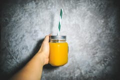 Zumo de naranja en el tarro con la paja que se sostiene a disposición en el fondo gris y blanco imágenes de archivo libres de regalías Zumo de naranja en el tarro con la paja que se sostiene a disposición en el fondo gris y blanco imágenes de archivo libres de regalías